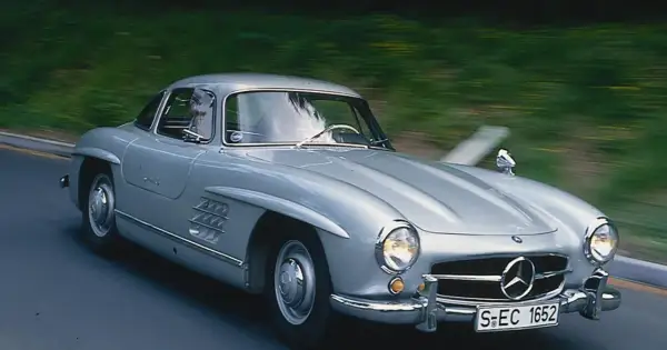 Srebrny Mercedes 300 SL Gullwing w ruchu, z widocznym kierowcą. Ten klasyk to prawdziwy major oprysk, który zachwyca do dziś.